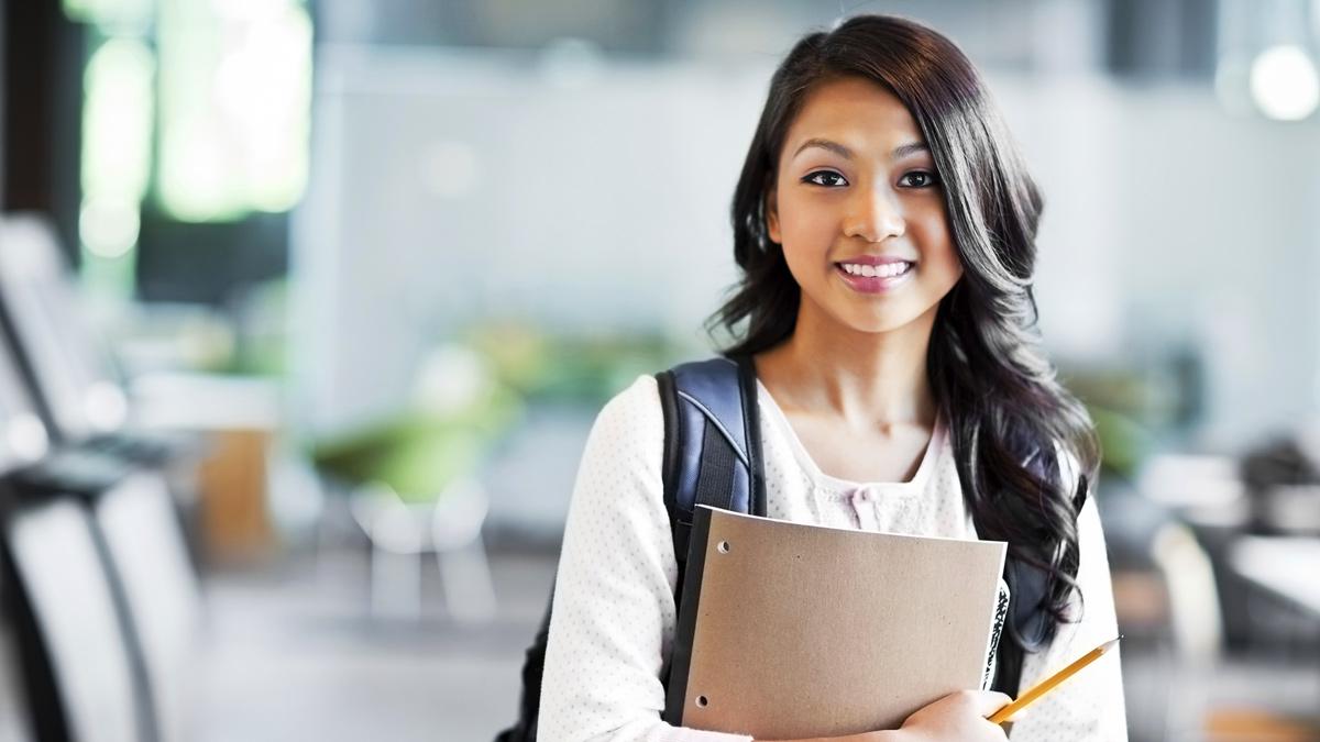 A student stands ready with her notebook and pencil in hand.