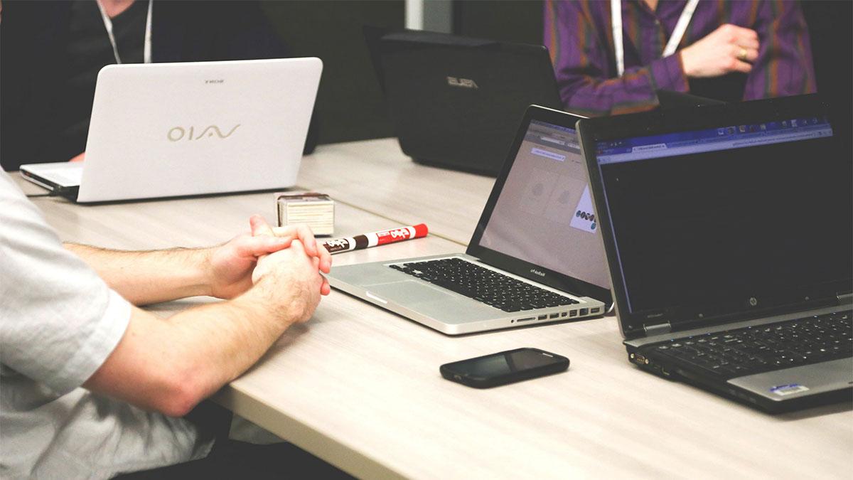 People meet with laptops on small table.