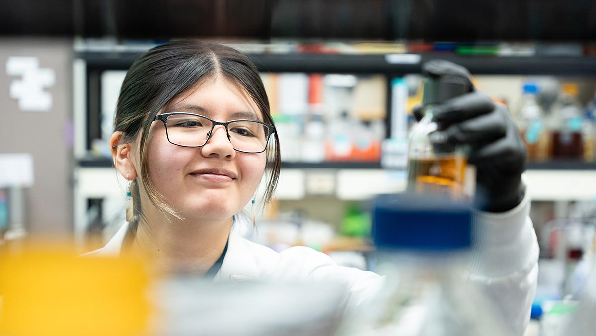 Smiling woman with glasses peers at a raised Petri dish.